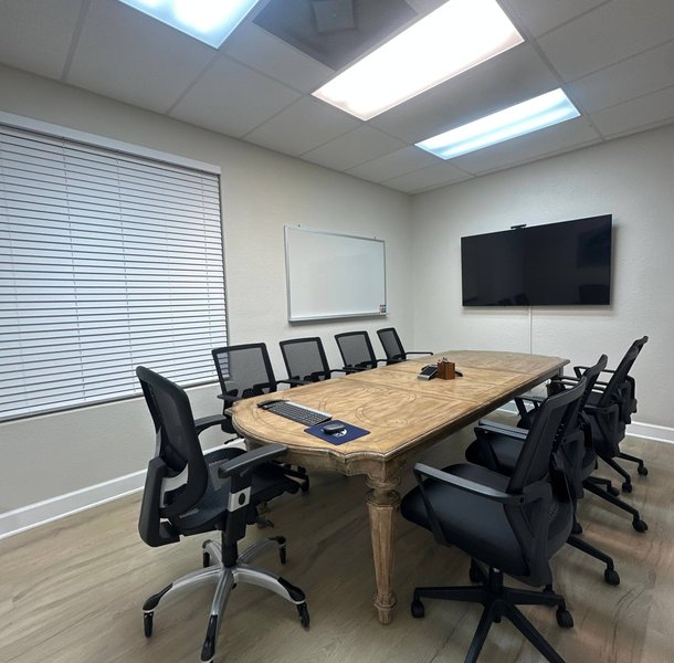 Conference room with wood table, mesh chairs, wall-mounted TV.