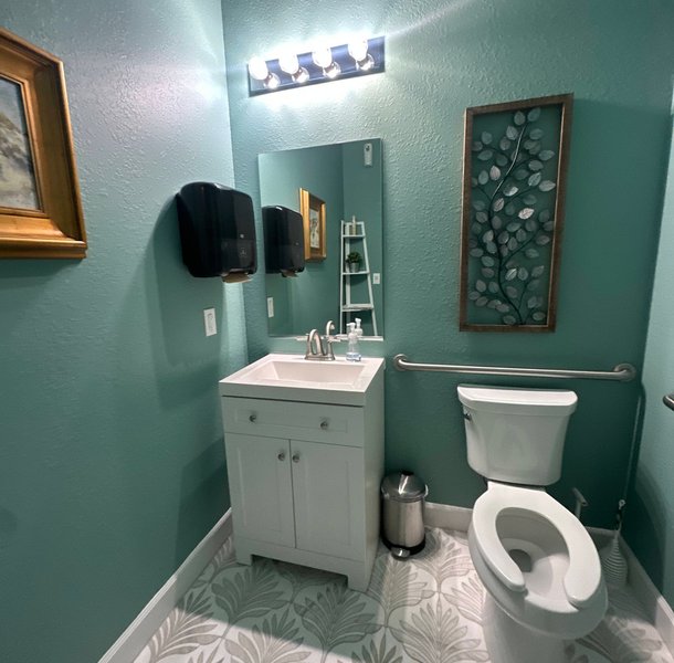 Teal bathroom with patterned floor, white vanity, leaf artwork.