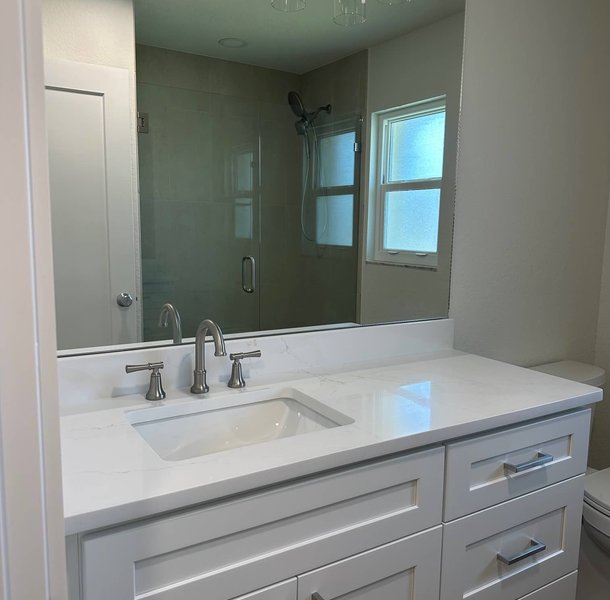White bathroom vanity with chrome fixtures, glass shower behind.