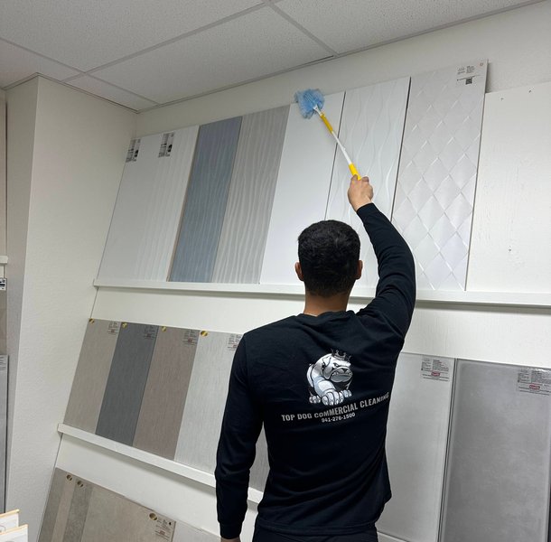 Worker dusting cabinet samples with extended duster in showroom.