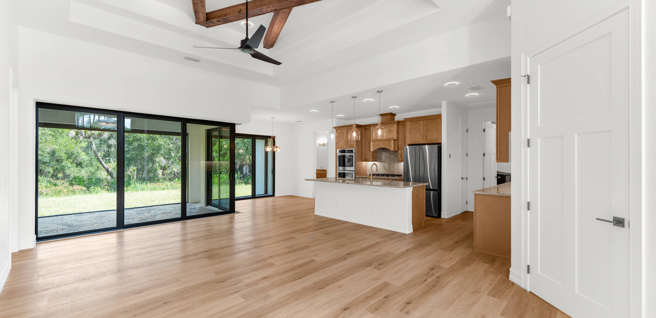 Open living space with wood beams, black-framed doors, kitchen.
