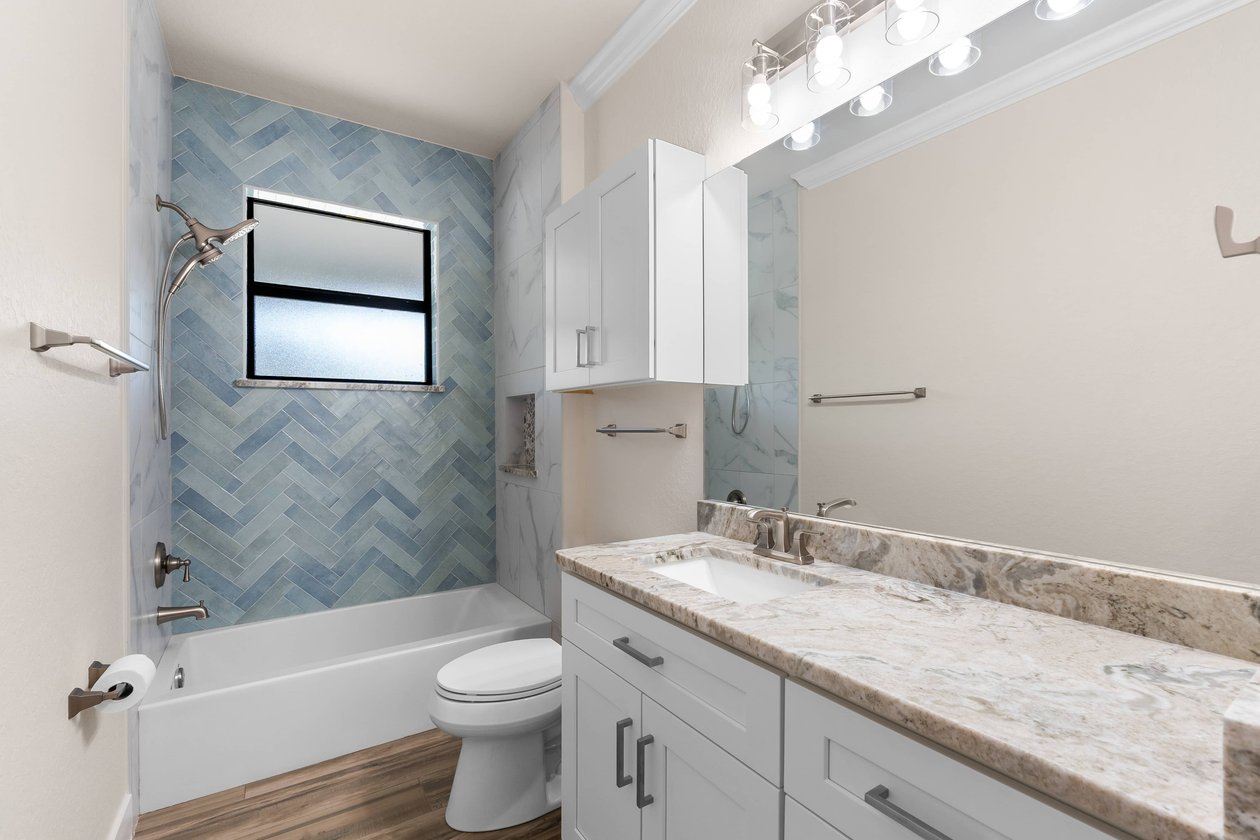Bathroom with blue herringbone tile, white vanity, marble counter.