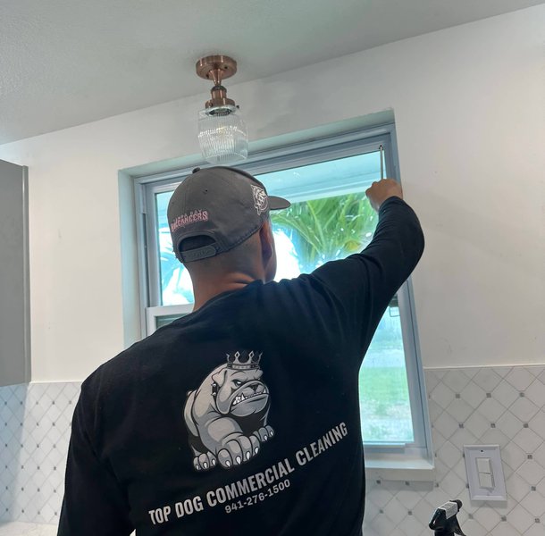 Worker cleaning window frame in bright white kitchen.