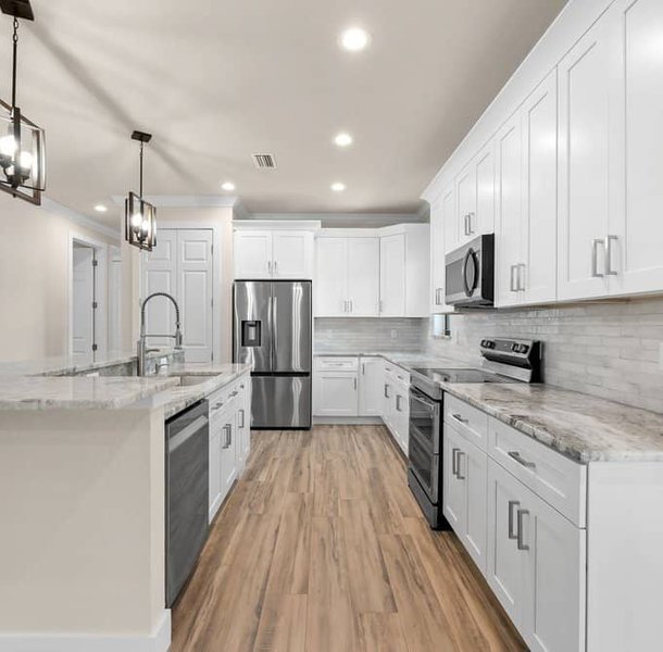 White kitchen with island, stainless appliances, wood-look flooring.