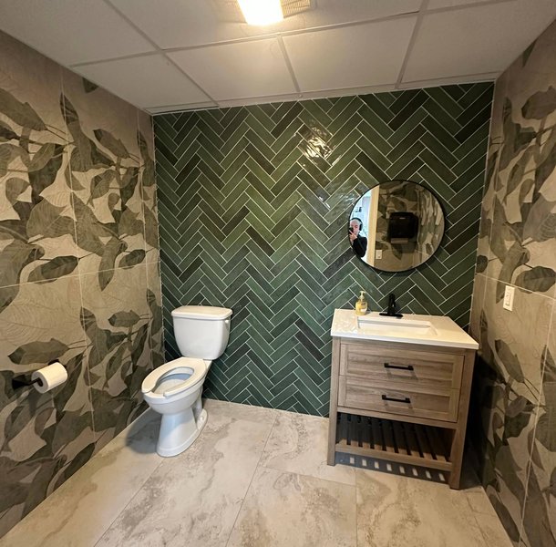 Bathroom with green herringbone tile, palm wallpaper, wood vanity.