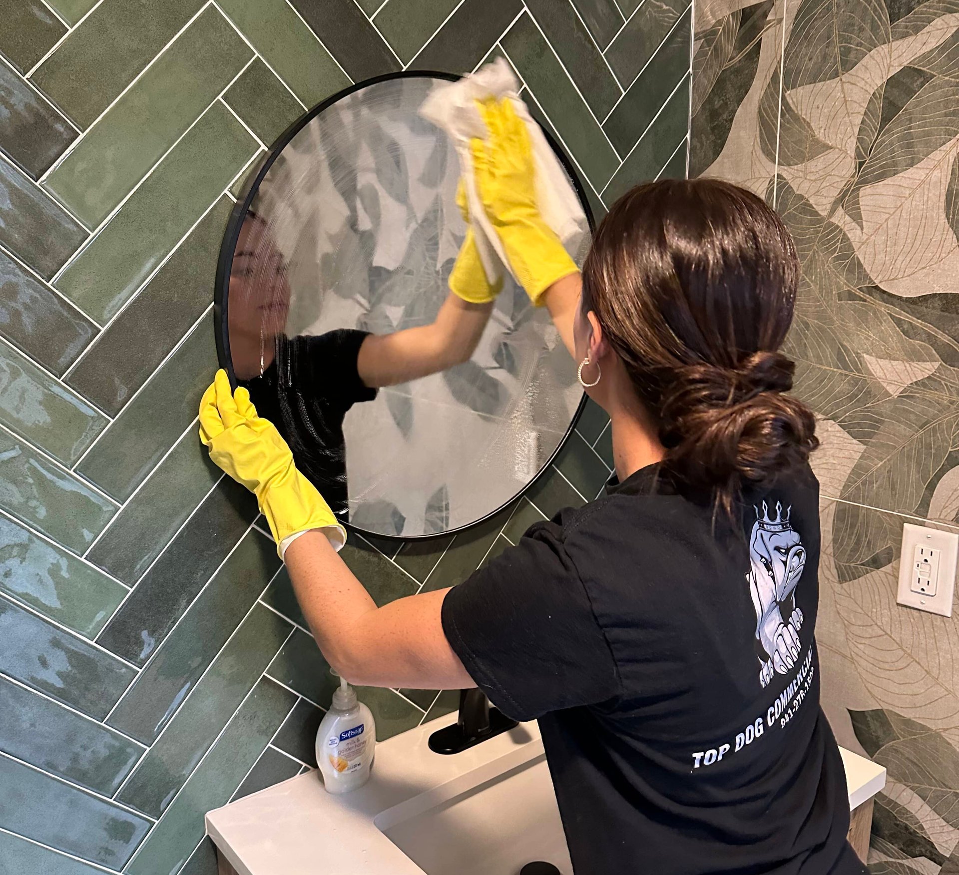Woman in yellow gloves cleaning bathroom mirror with spray.